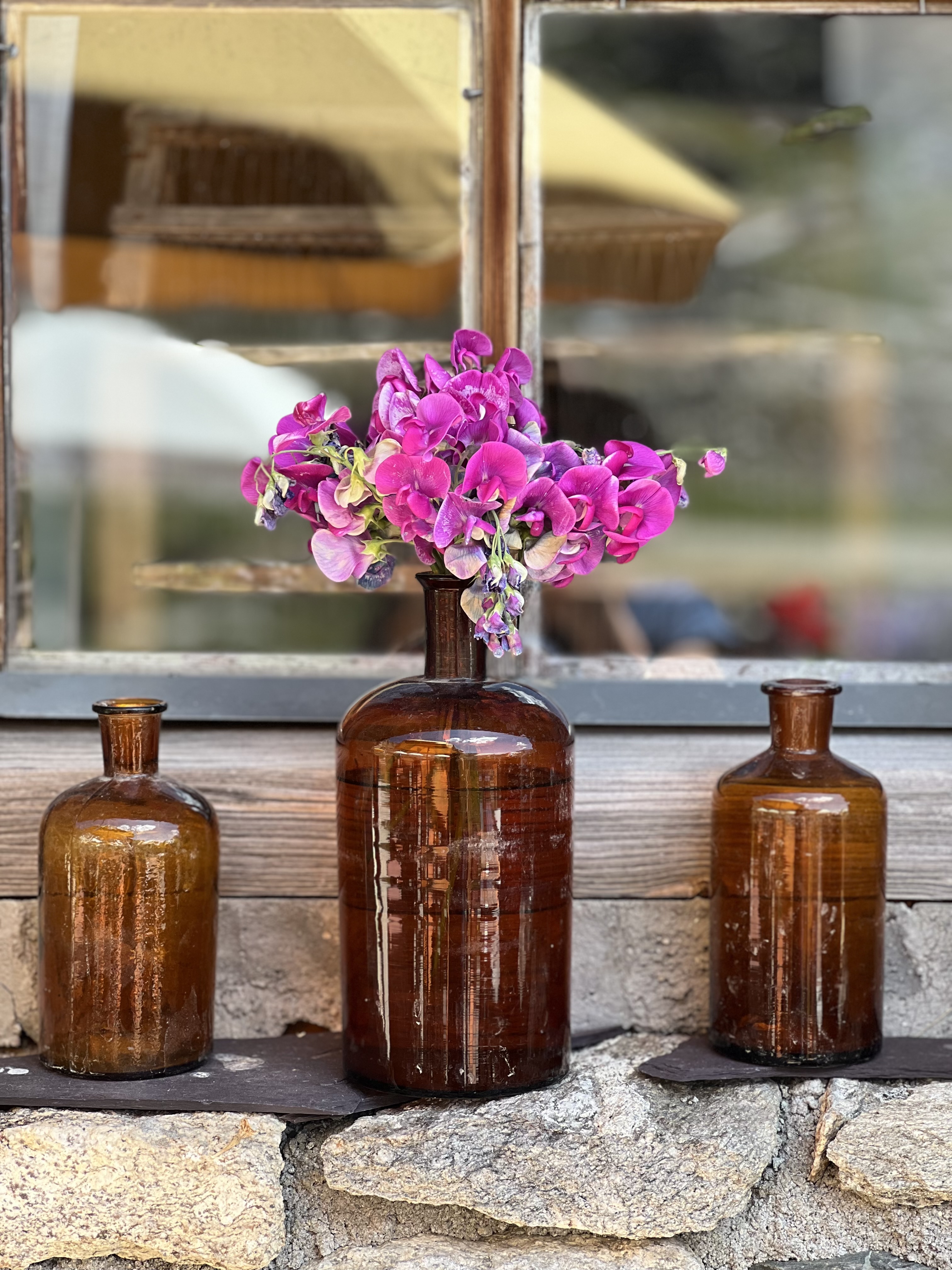 Braune Flaschen mit lila Blumen auf Steinmauer